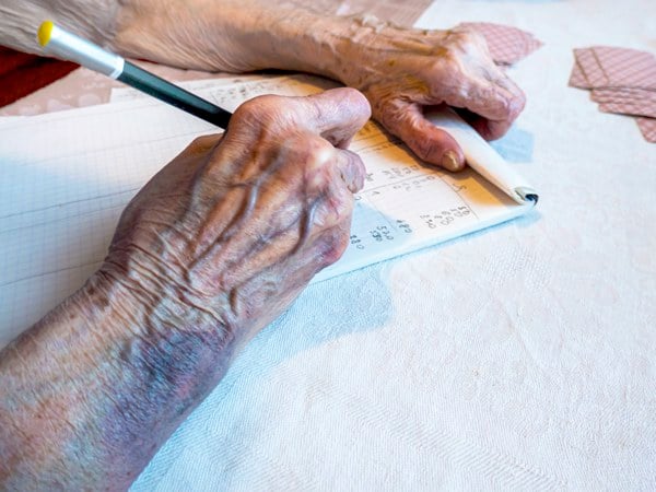 the hand of an elderly woman with bruises write the score in a card game